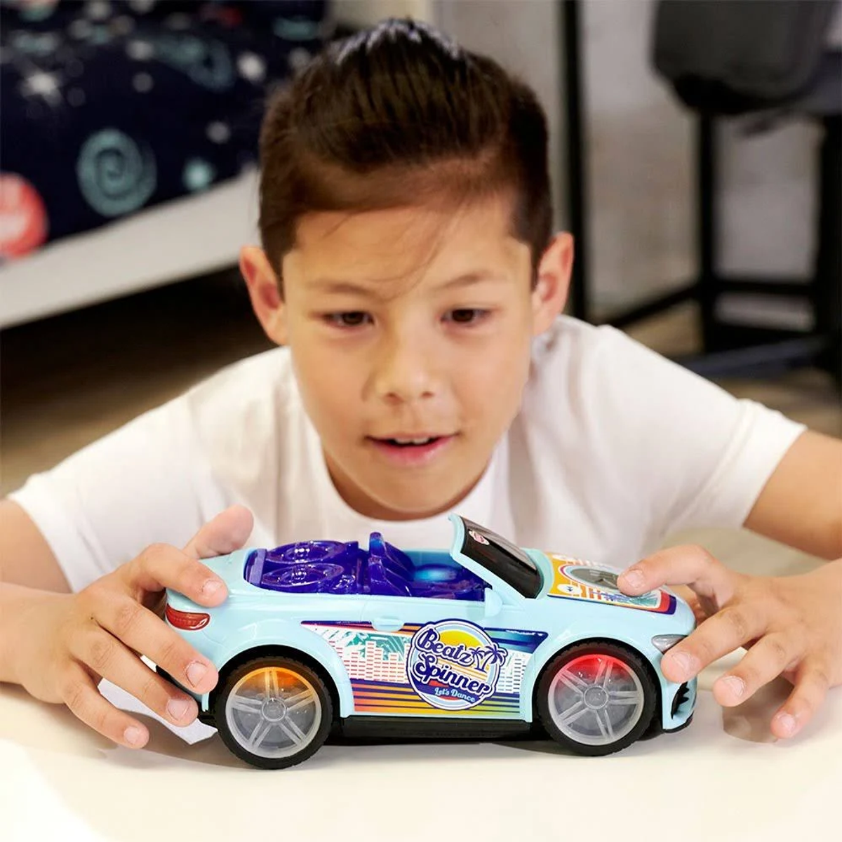 Junge hält Spielzeugauto, hellblaues Cabrio mit bunten Grafiken.