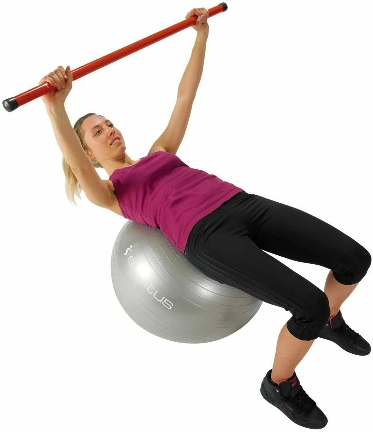 Donna su una palla da ginnastica grigia, che tiene una barra rossa sopra la testa.