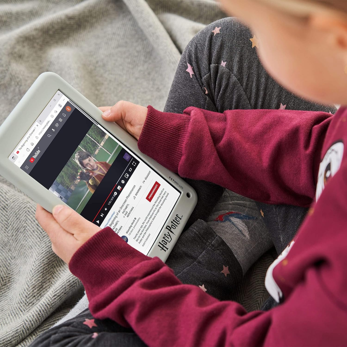 Una bambina tiene in mano un tablet con un video in riproduzione, seduta su un letto.