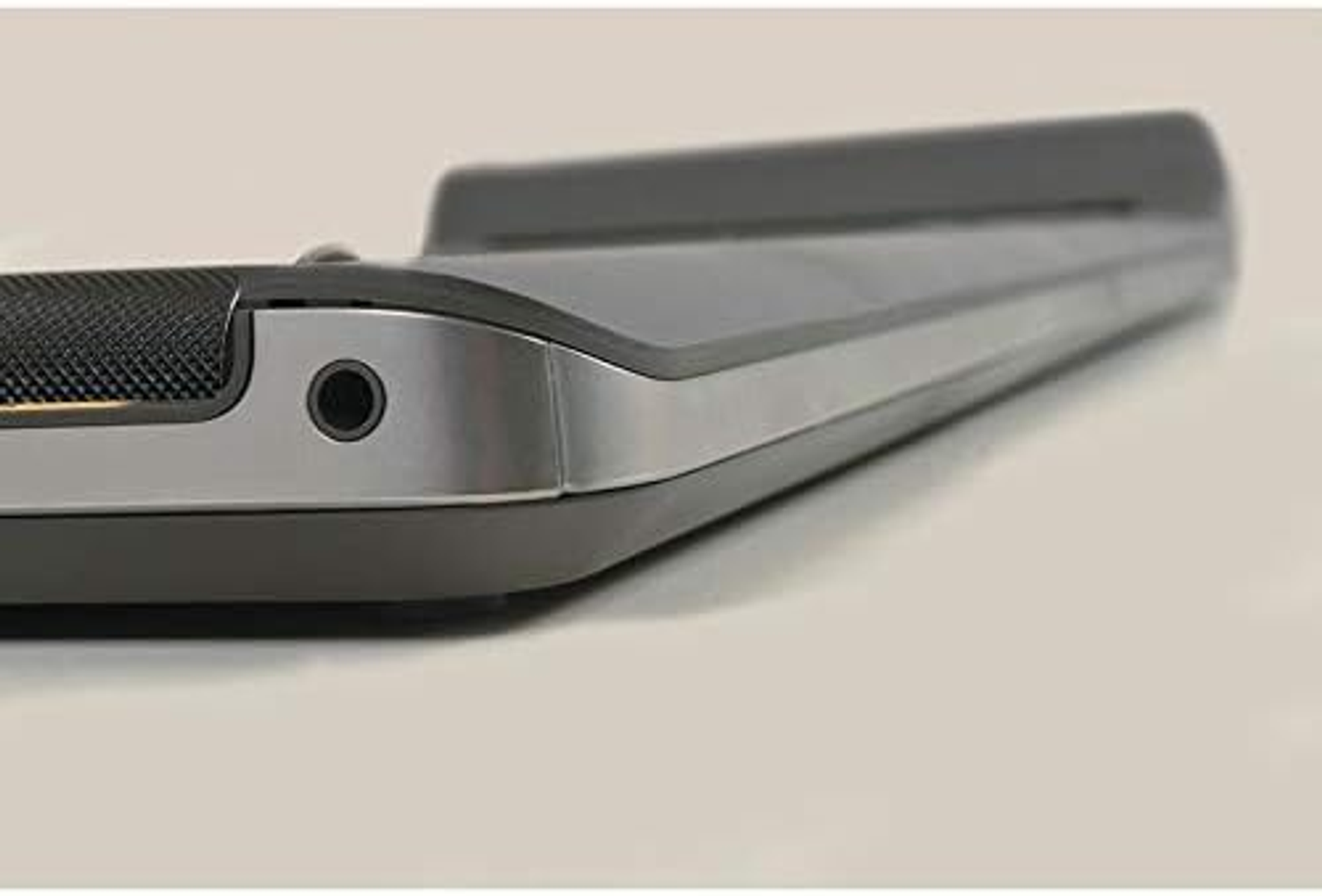 Close-up of a soundbar. Black with silver trim, audio jack visible. Angled view, white background.