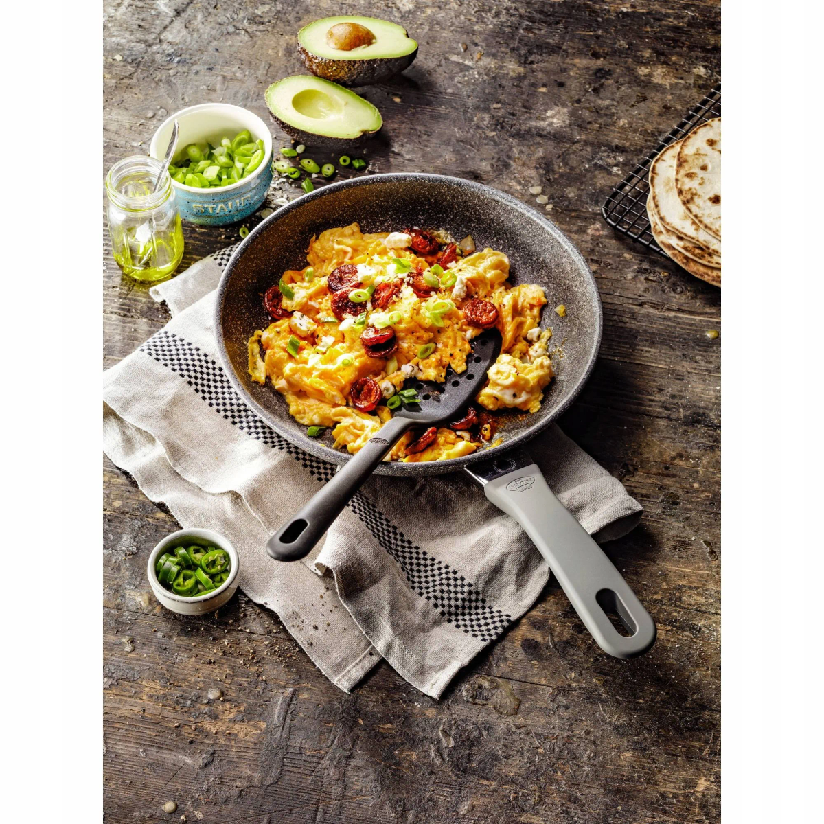 Rührei mit Chorizo in einer Pfanne, mit Avocado, Tortillas und weiteren Zutaten.