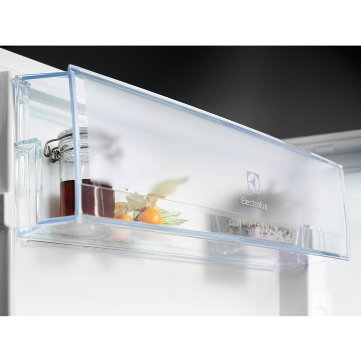 Cajón de refrigerador con tarro de conservas y fruta. Plástico transparente. Interior blanco.