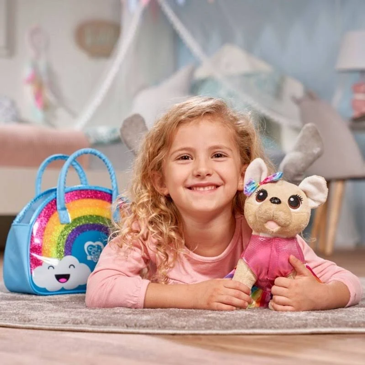 Niña sosteniendo un perro de juguete, sonriendo. Una bolsa de arcoíris a la izquierda. El fondo es un dormitorio.