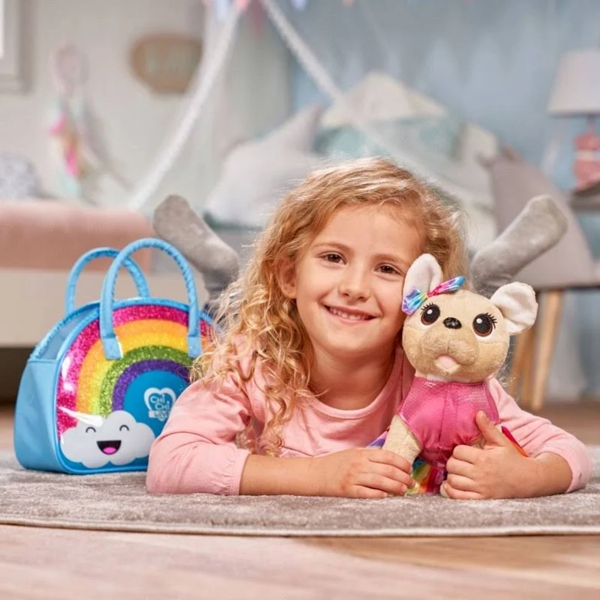 Niña con perro de juguete y bolso. La niña sonríe, vestida de rosa. El bolso tiene un arcoíris y una nube.