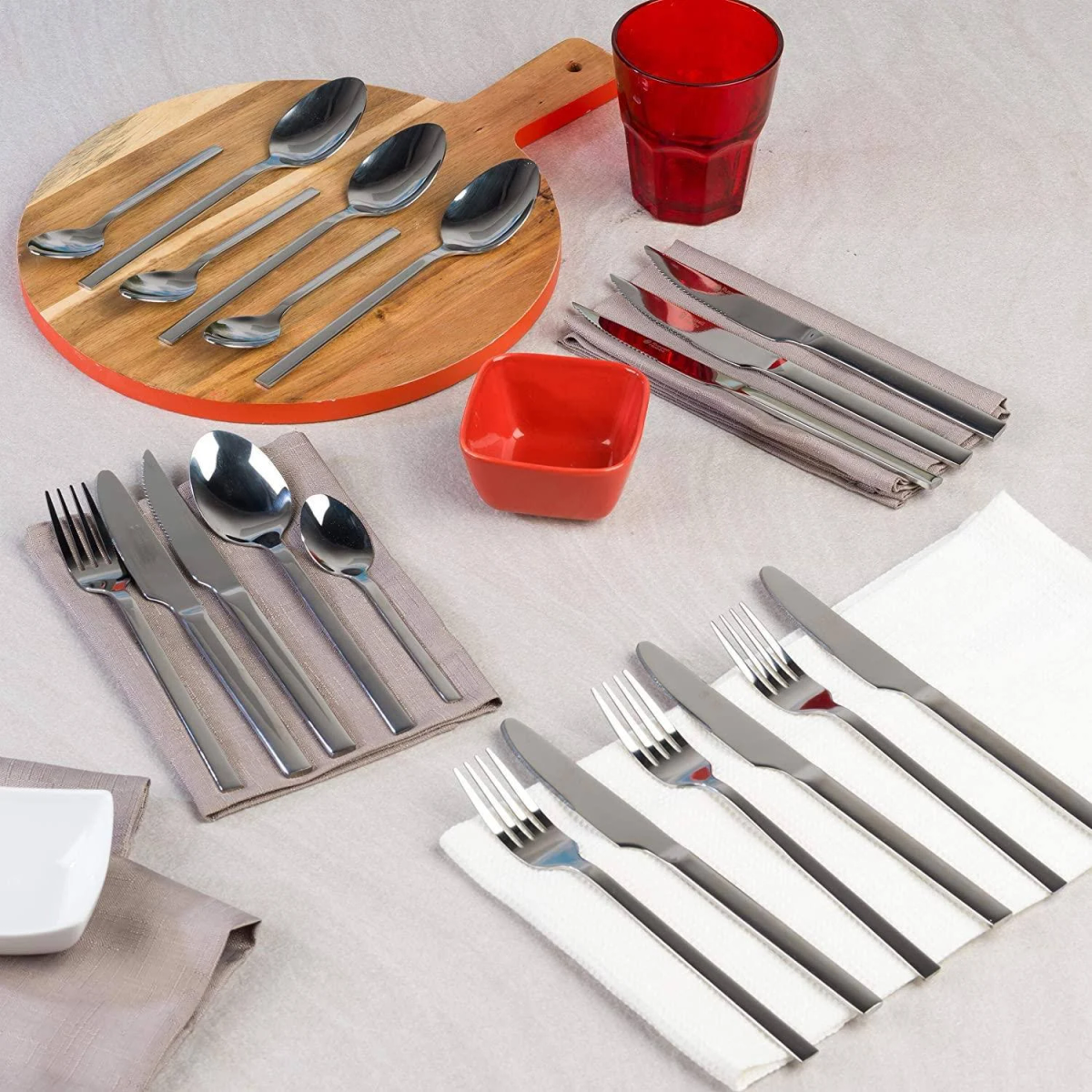 Tischgedeck mit Besteck, roter Schale und Glas. Besteck auf Servietten. Holzservierbrett.