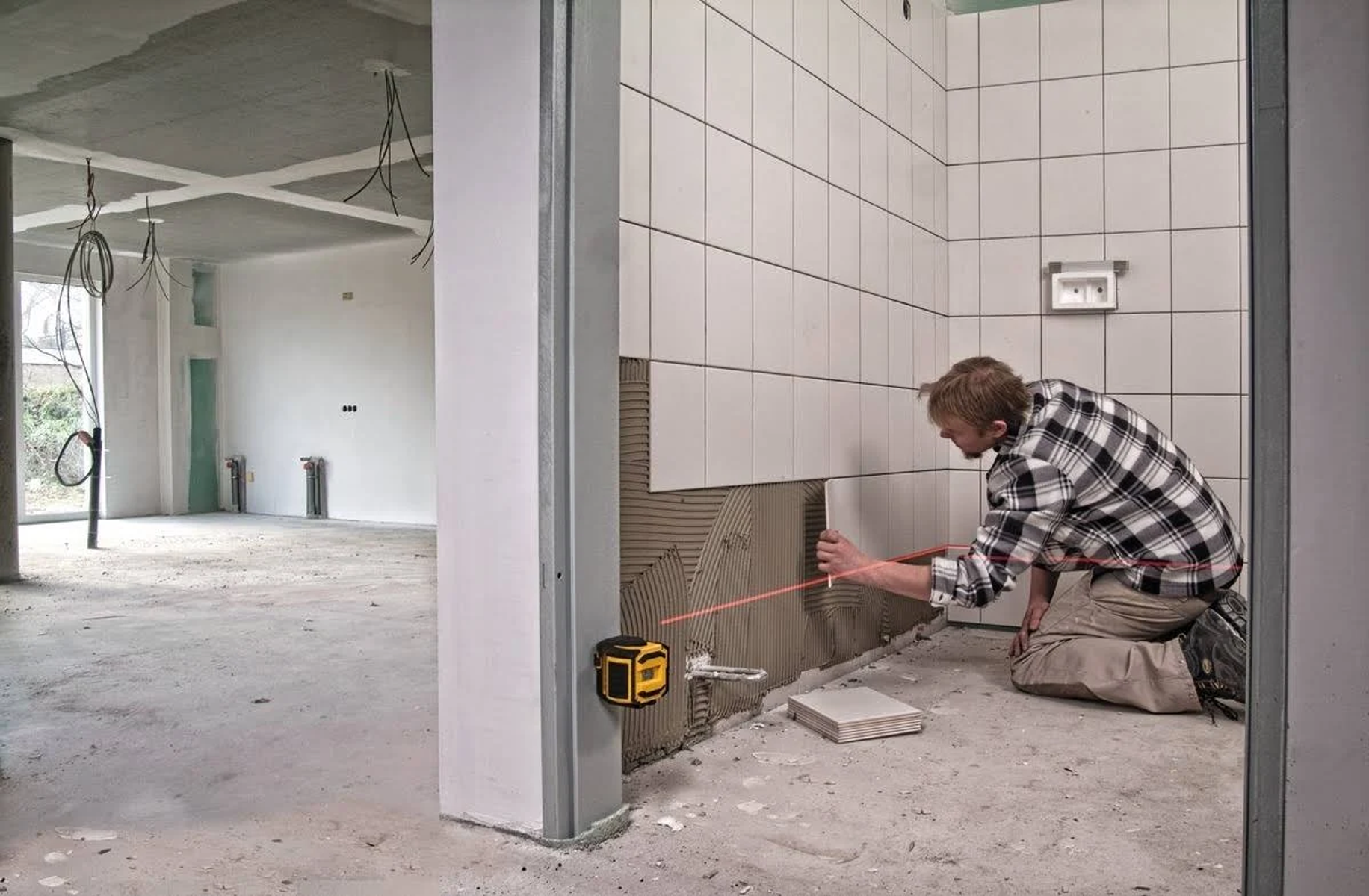Uomo che installa piastrelle con un livella laser in un cantiere.