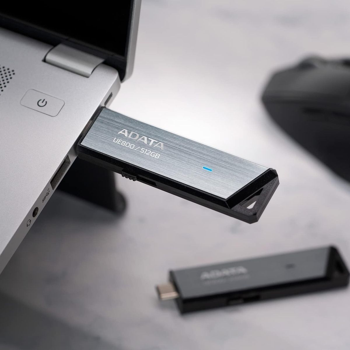 Clé USB argentée branchée sur un ordinateur portable. Une autre clé est sur la table.
