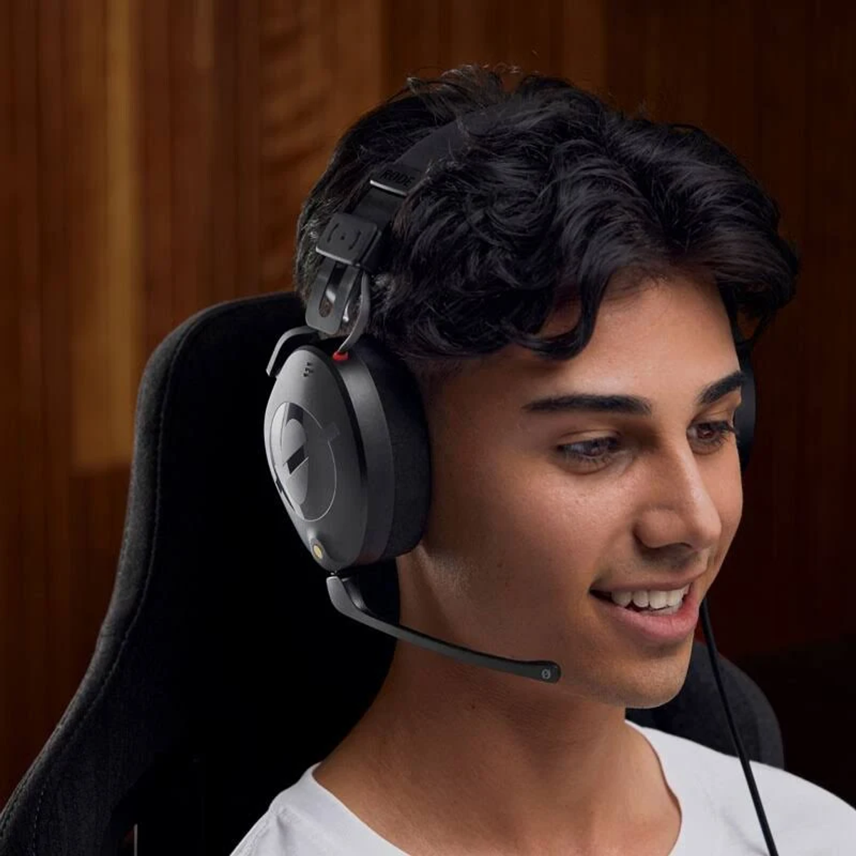 Ein junger Mann mit einem schwarzen Gaming-Headset mit Mikrofon, lächelnd. Er sitzt in einem Gaming-Stuhl.