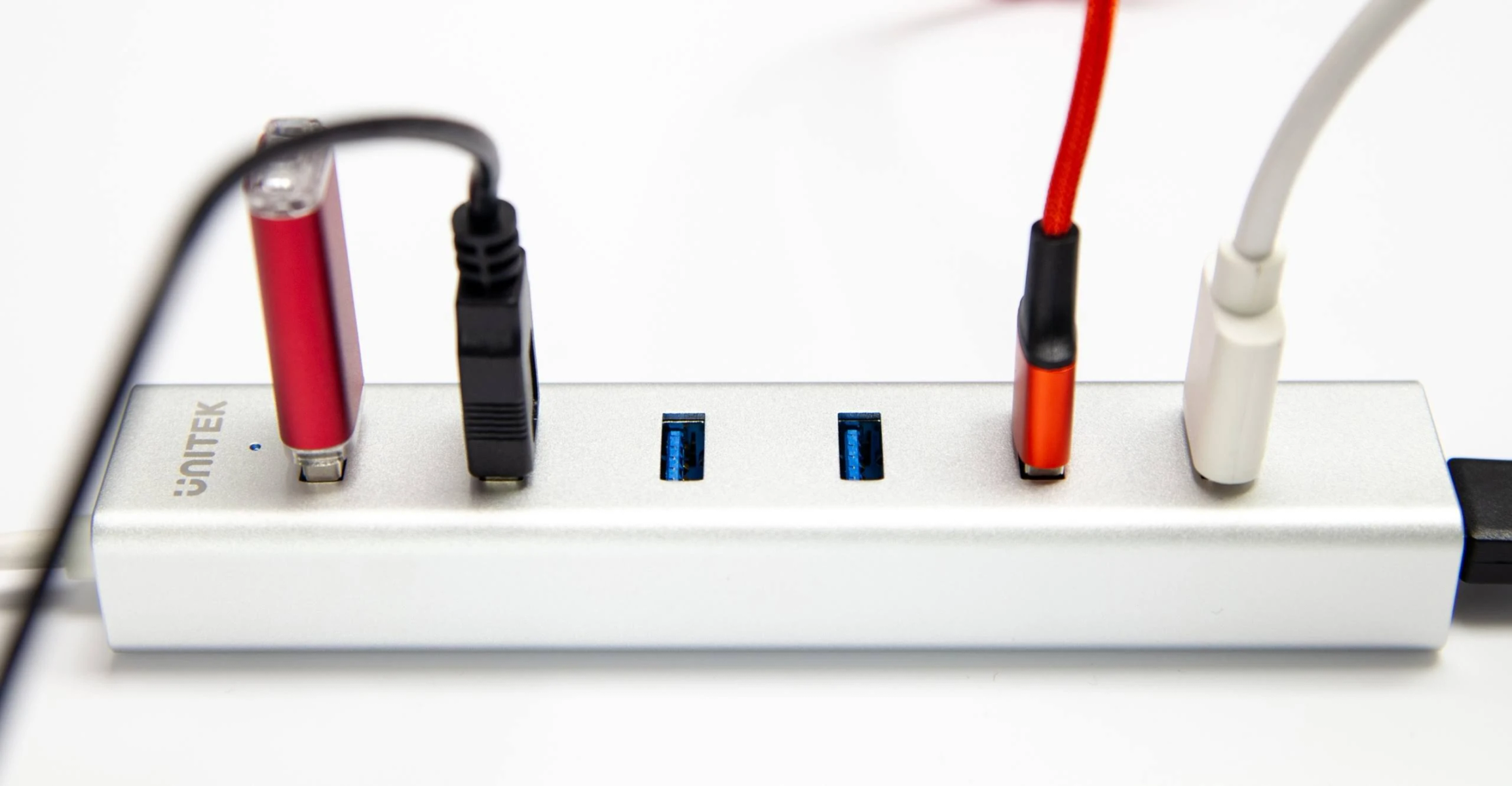 Ein silberner USB-Hub mit mehreren angeschlossenen Kabeln, darunter rote, schwarze und weiße.
