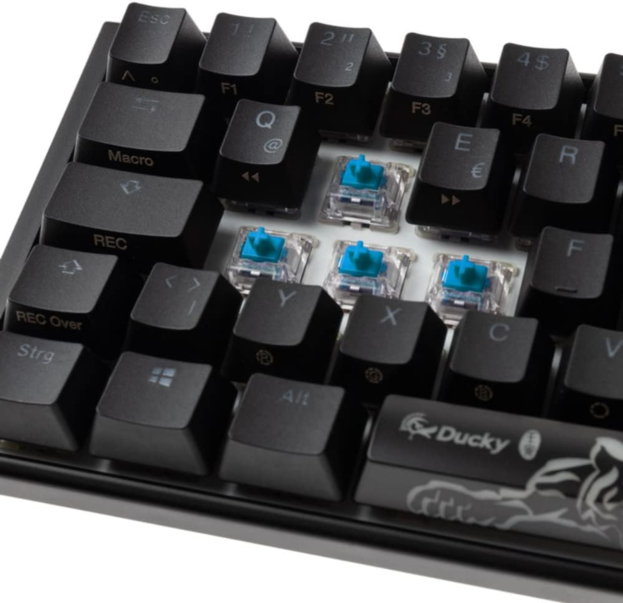 Tastiera nera con tasti mancanti, che mostra interruttori blu. Logo Ducky visibile.