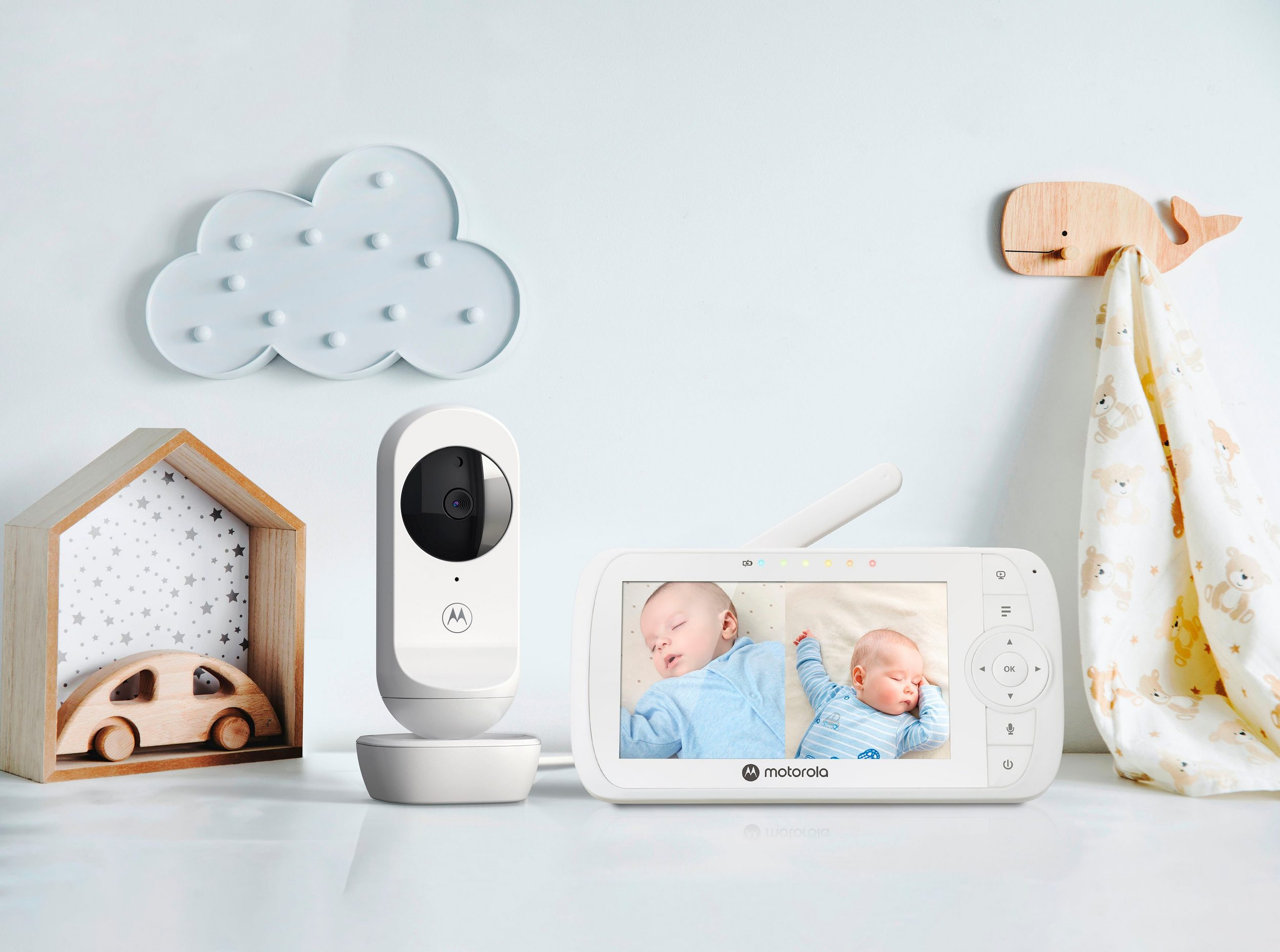 Baby monitor showing two babies sleeping. Wooden toys and cloud decoration are on the side.