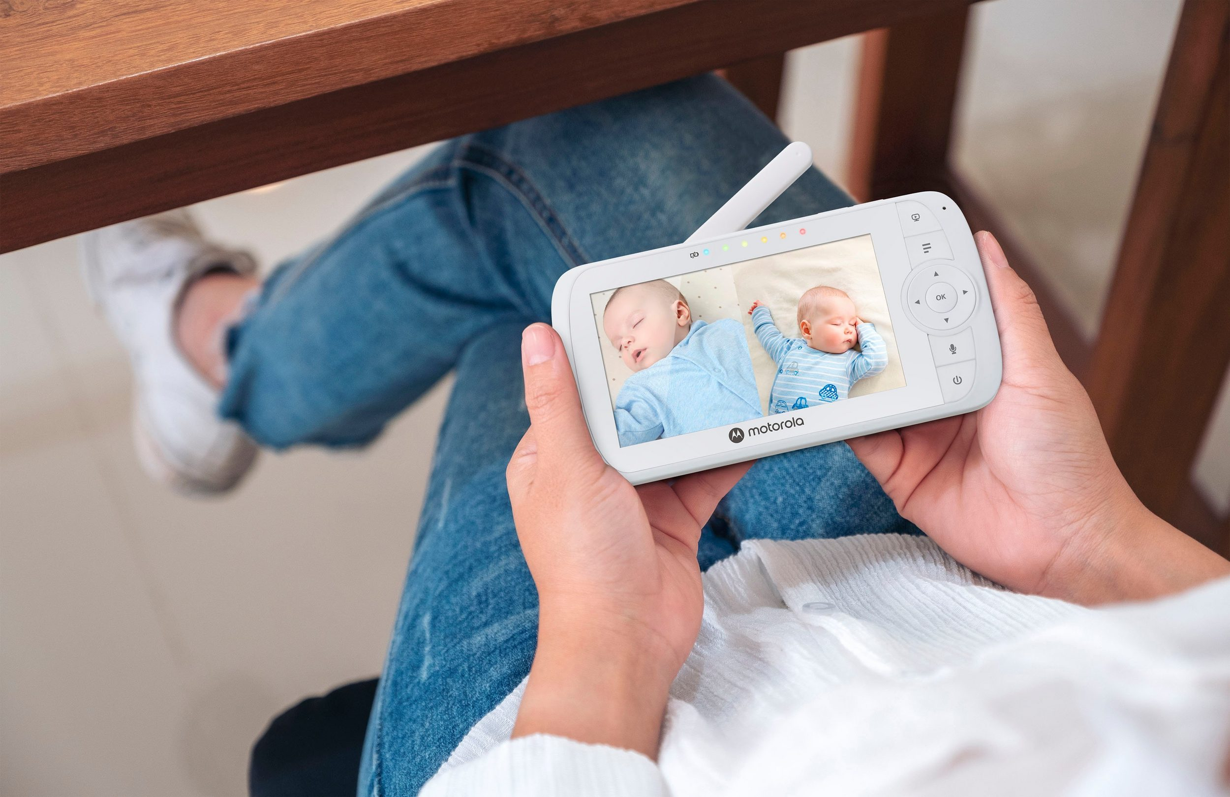 Hands holding a Motorola baby monitor showing two sleeping babies on the screen.