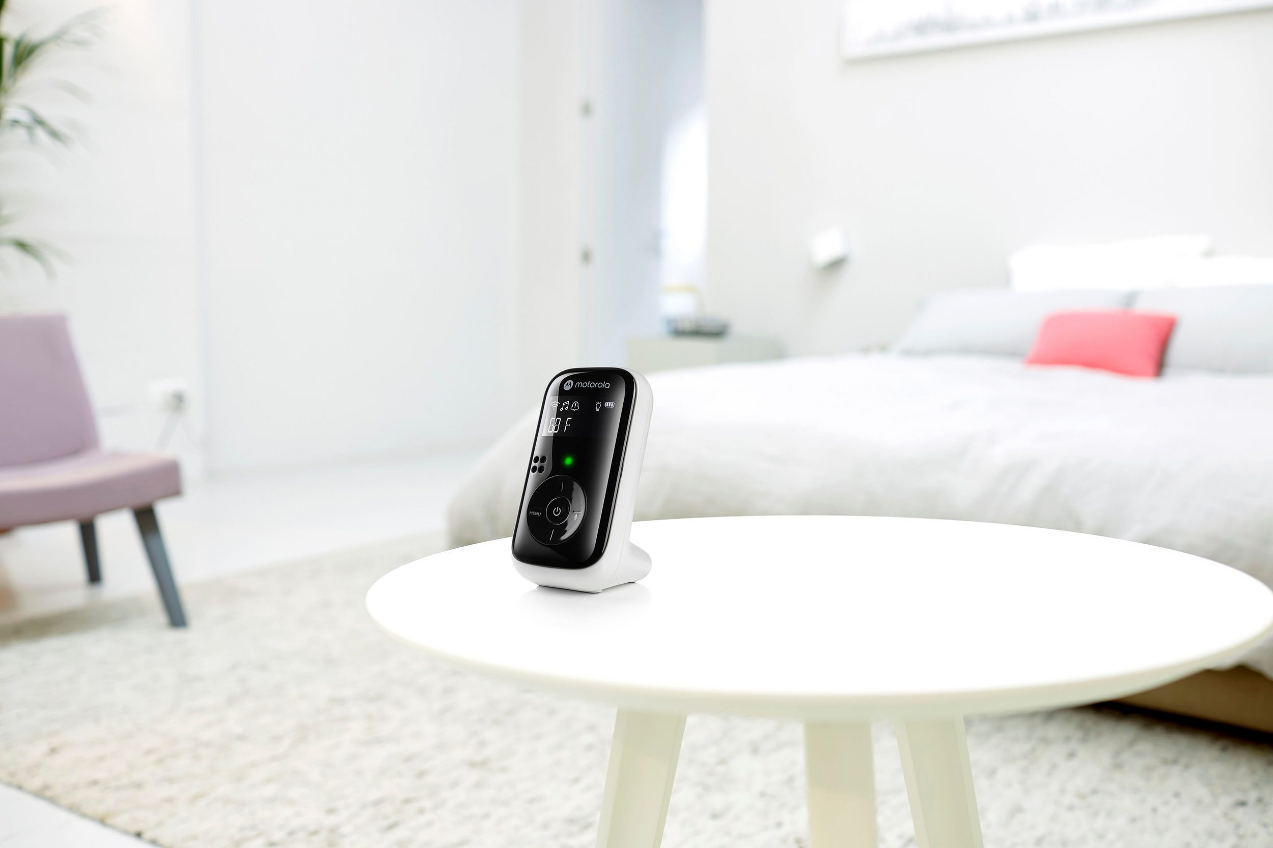 Babyphone auf einem weißen Tisch im Schlafzimmer. Bett und Stuhl im Hintergrund.