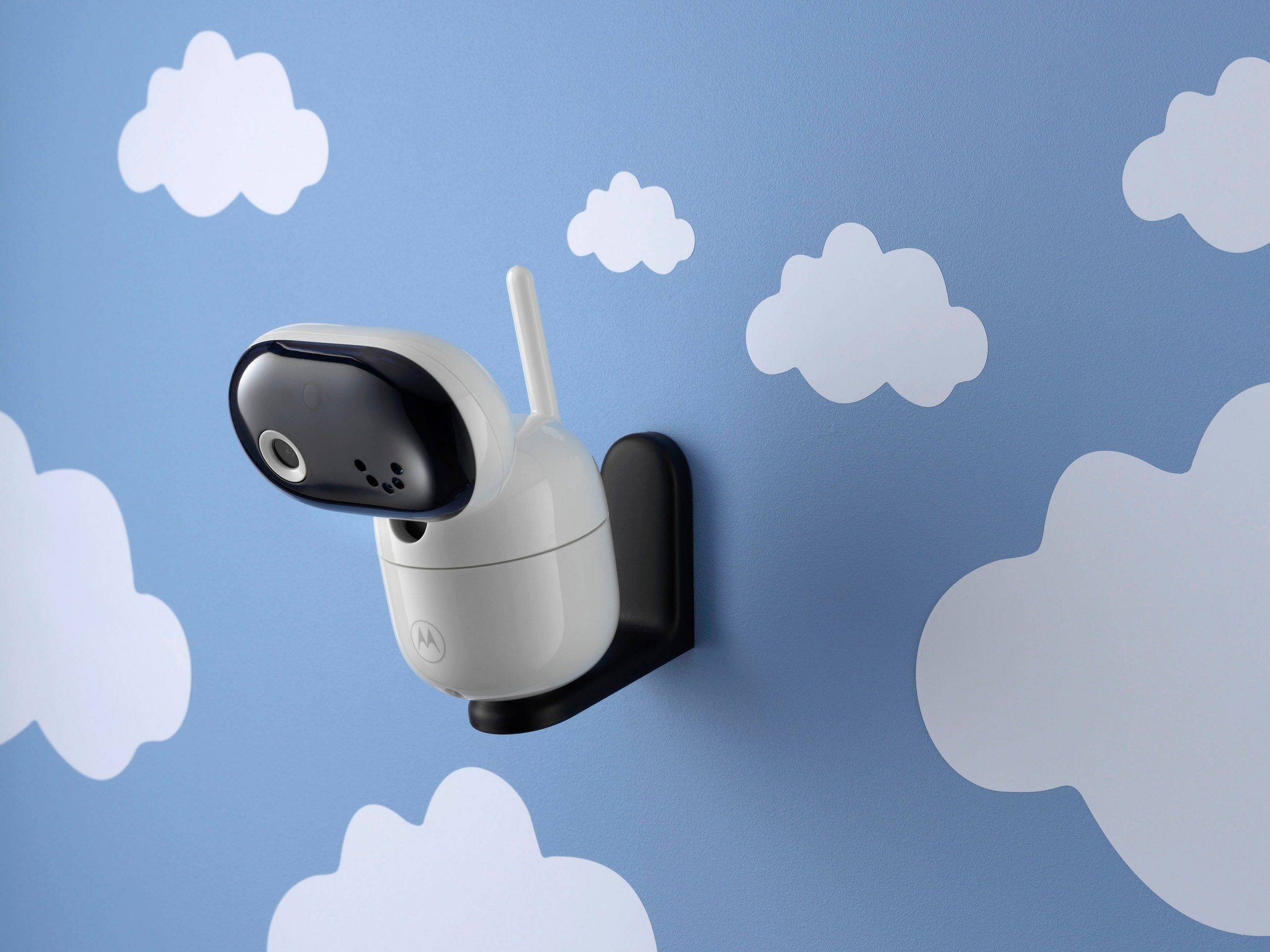 Weißer und schwarzer Babyphone an einer blauen Wand mit weißen Wolkenaufklebern befestigt.