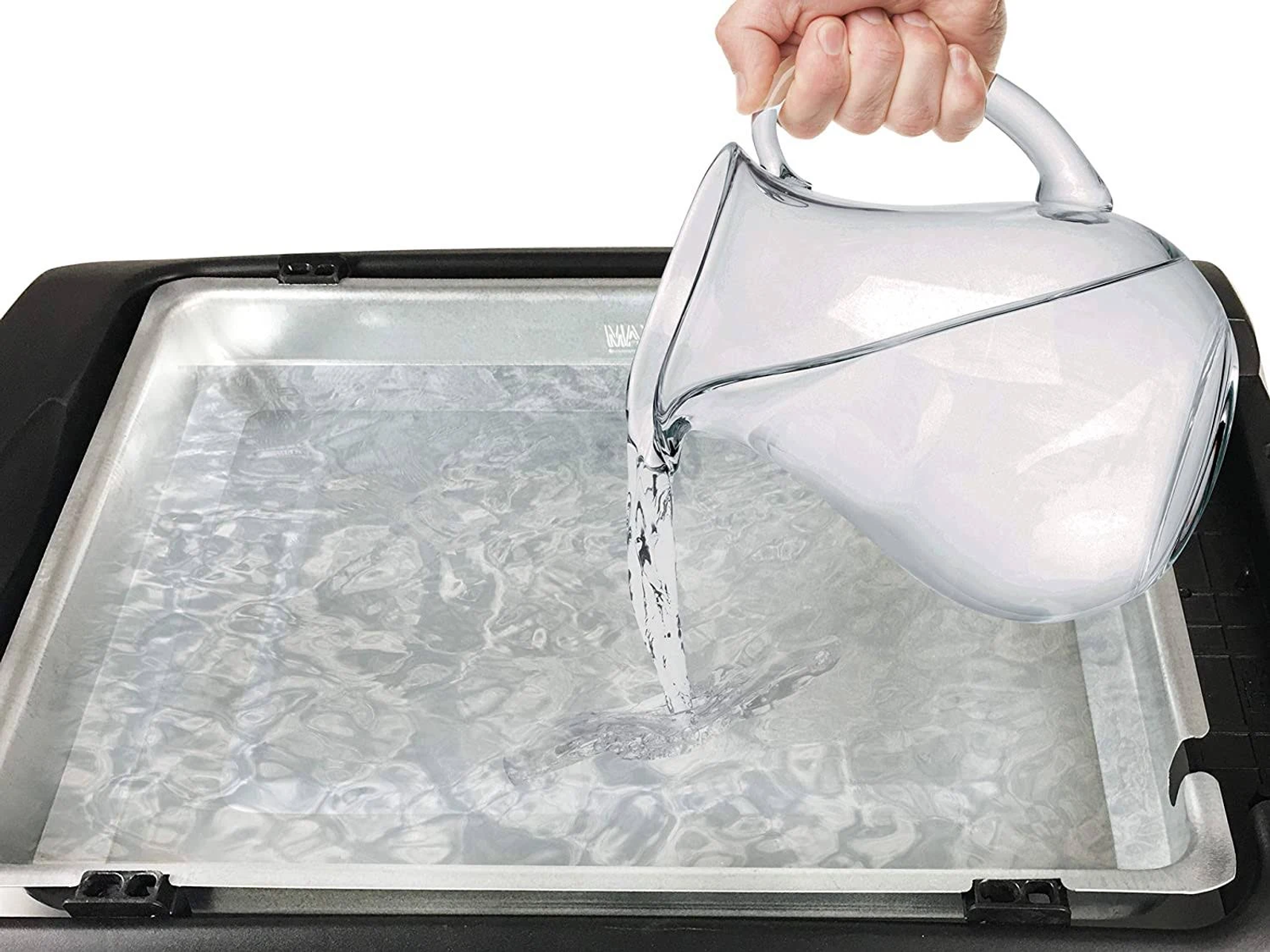 Ręka wlewa wodę do przezroczystego pojemnika na czarnej powierzchni.