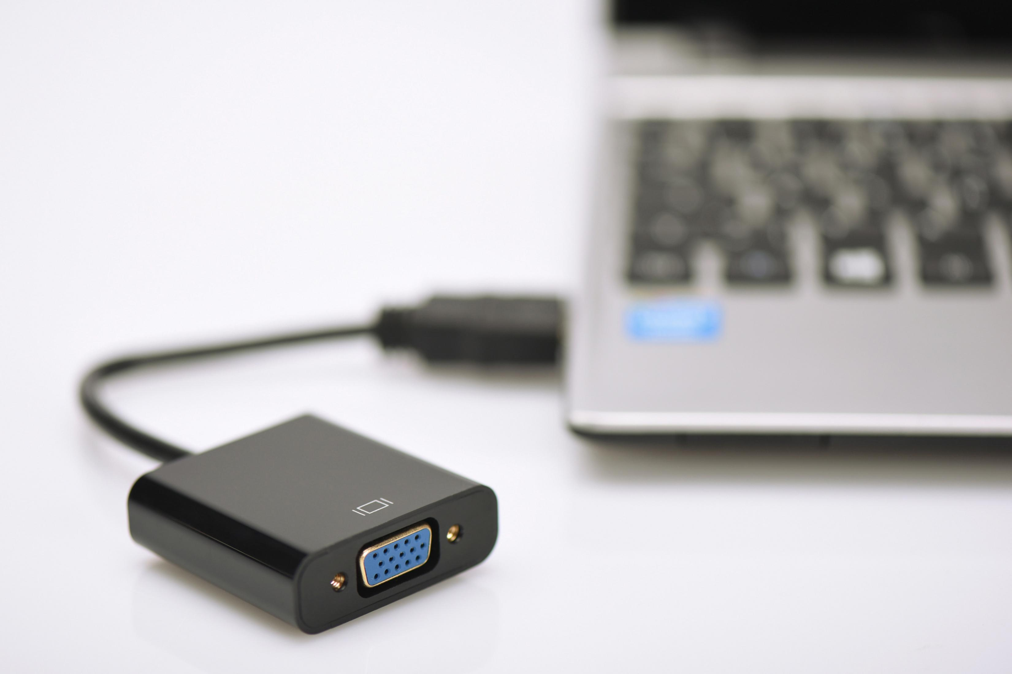 Schwarzer VGA-Adapter, der an einen Laptop angeschlossen ist. Der Adapter befindet sich auf einer weißen Oberfläche.