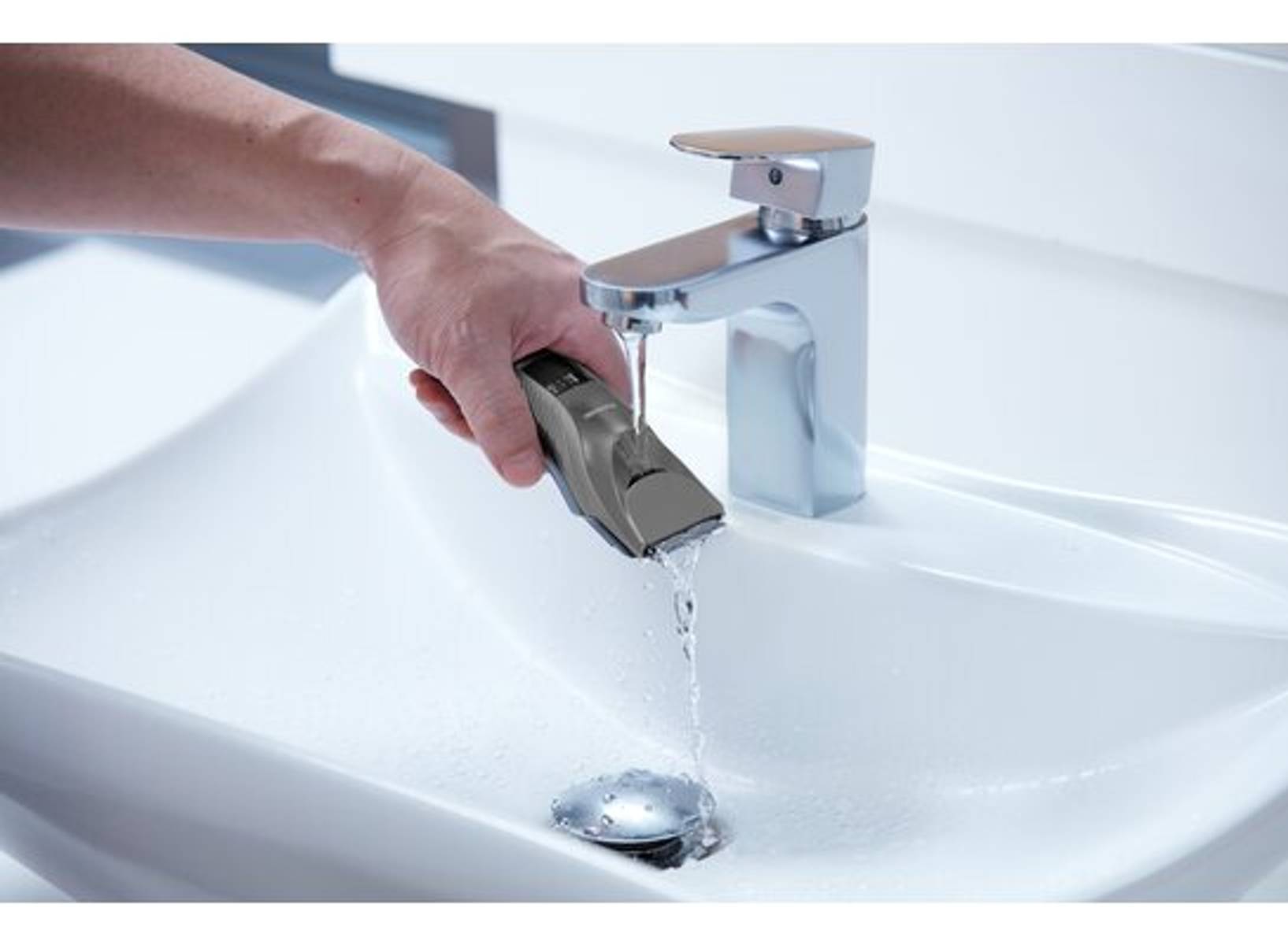 Mano che usa un tagliacapelli sotto l'acqua corrente in un lavandino.