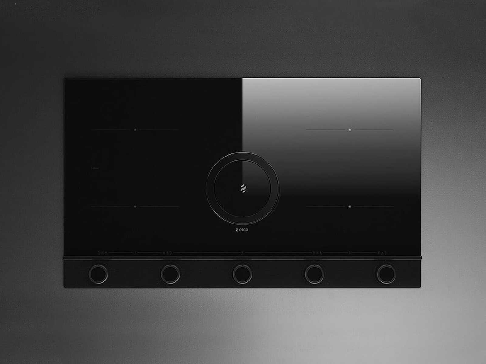 Piano cottura nero con cinque zone cottura. Ha un design circolare centrale.