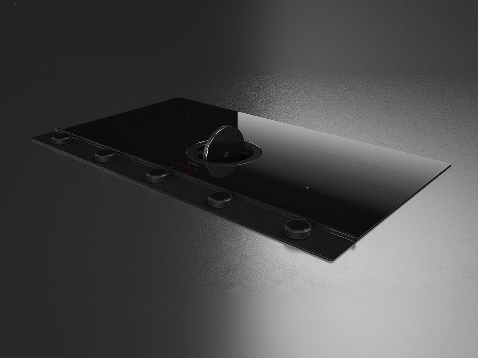 Piano cottura nero con sistema di ventilazione integrato. Quattro manopole di controllo e un'aerazione centrale. Sfondo scuro.