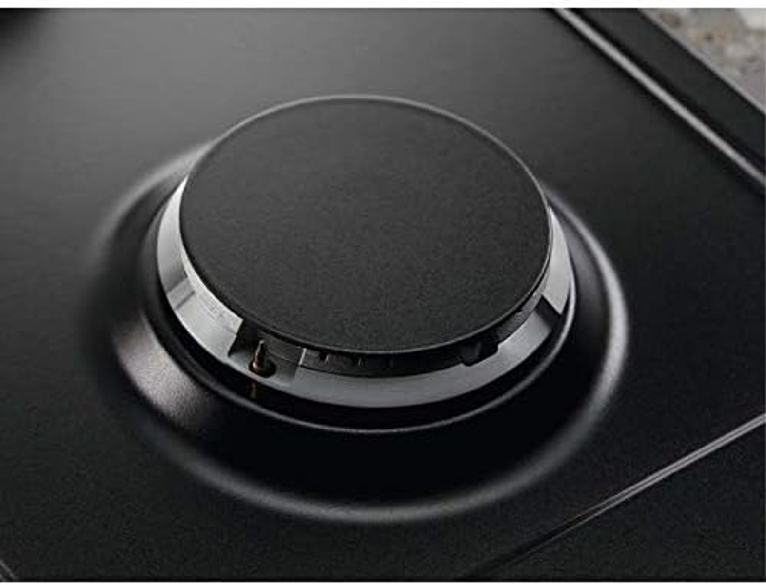 Zbliżenie czarnego palnika na płycie grzewczej. Jest włączony i ma metalowy pierścień.