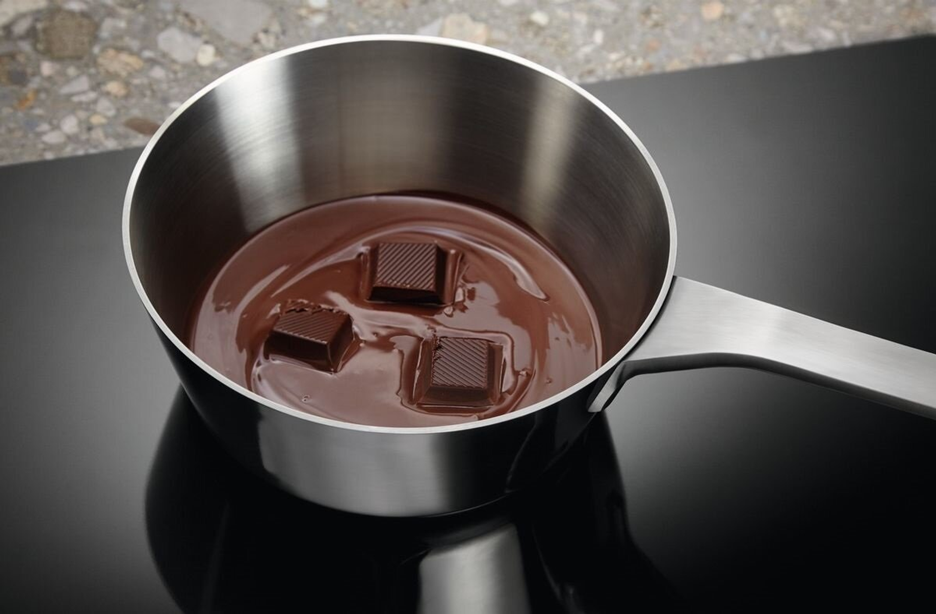 Garnek ze stali nierdzewnej z roztopioną czekoladą i kostkami czekolady.