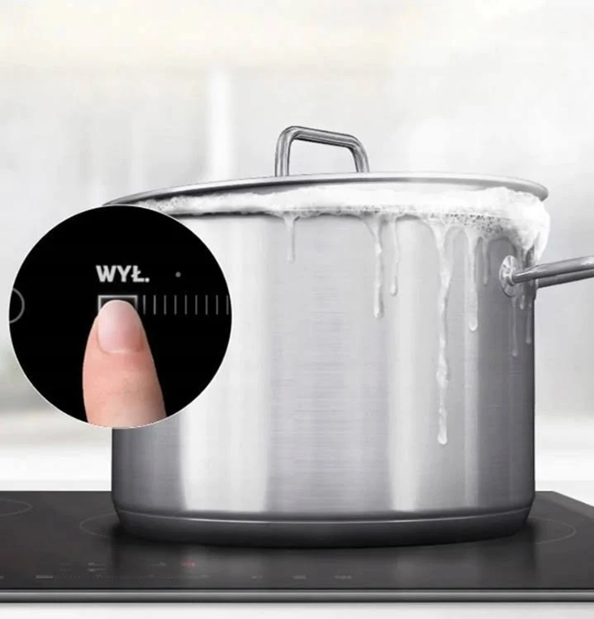 Un dedo presiona el botón 'WYŁ' en una placa de inducción negra junto a una olla hirviendo.