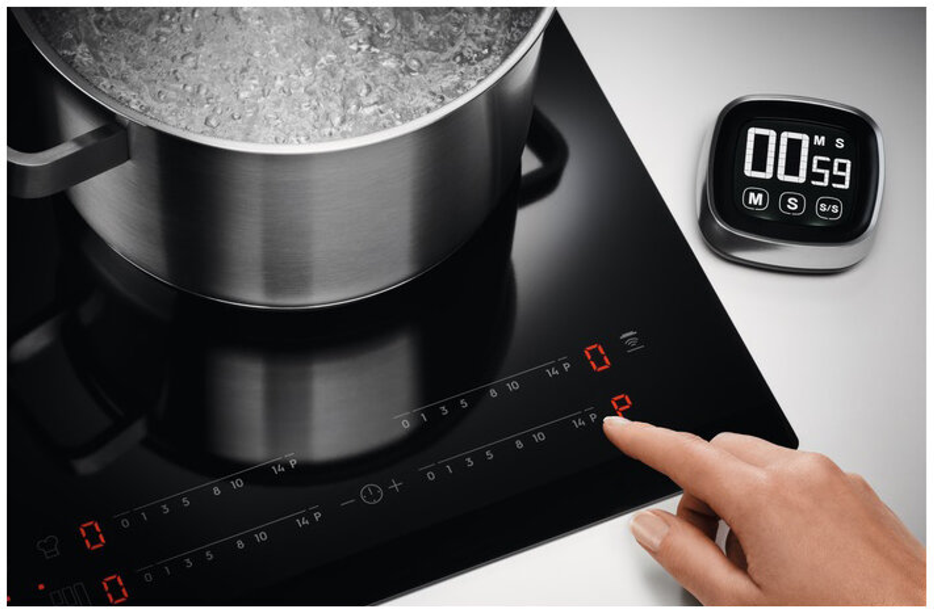 Ręka dotyka czarnej płyty indukcyjnej, garnek gotuje się z timerem w tle.