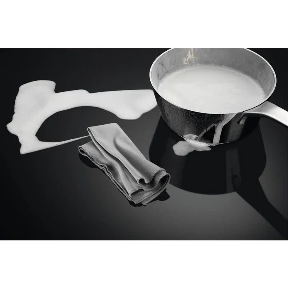 Latte che esce da una pentola, con un panno su un piano cottura nero, creando schiuma.