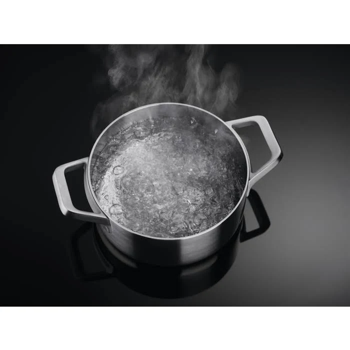 Una pentola in acciaio inossidabile con acqua bollente su un piano cottura nero. Il vapore sale dall'acqua.