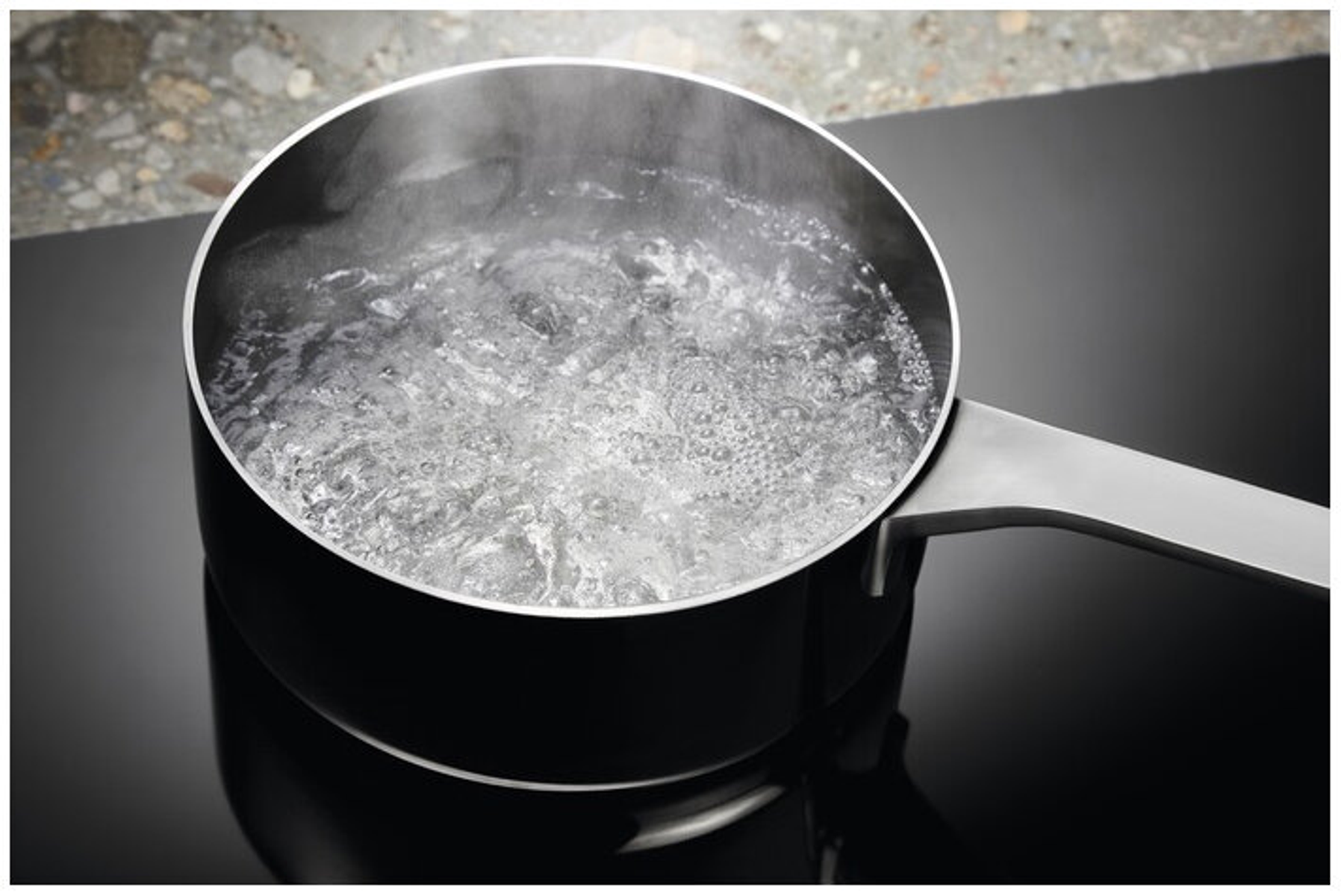Garnek wrzącej wody na czarnej płycie grzewczej. Para unosi się z wody.