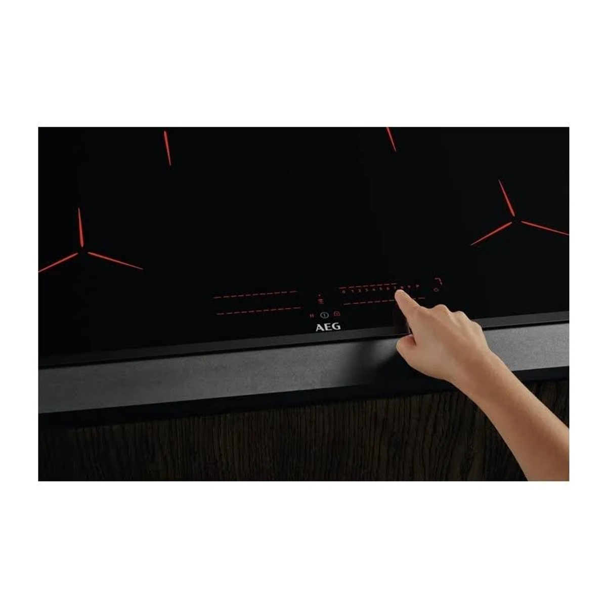 Una mano che tocca i comandi touch di un piano cottura a induzione nero, con zone cottura illuminate di rosso.