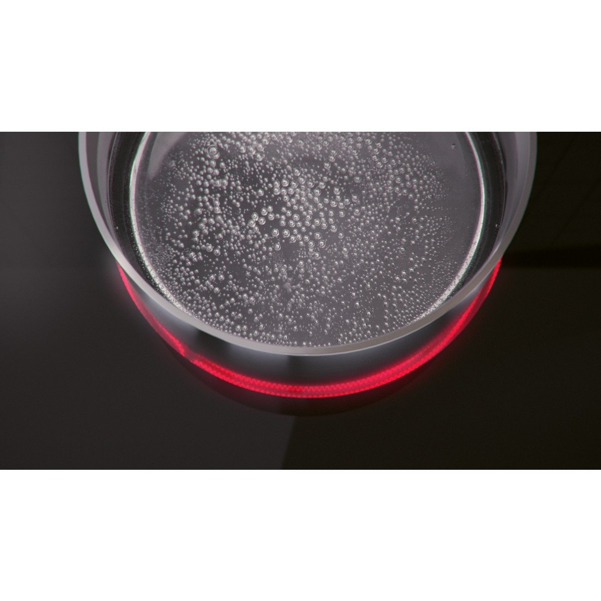 Woda wrze na czarnej płycie indukcyjnej z czerwonym wskaźnikiem ciepła.