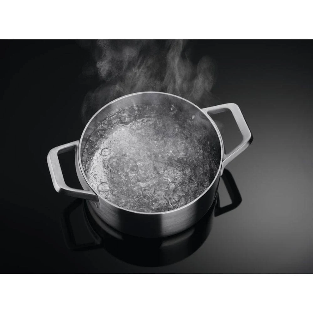 Una pentola in acciaio inox con acqua bollente su un piano cottura nero.