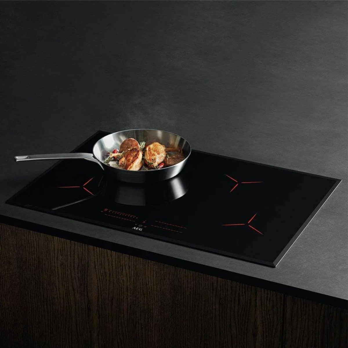 Un piano cottura a induzione nero con una padella di cibo e una spatola sopra, con una superficie in legno.