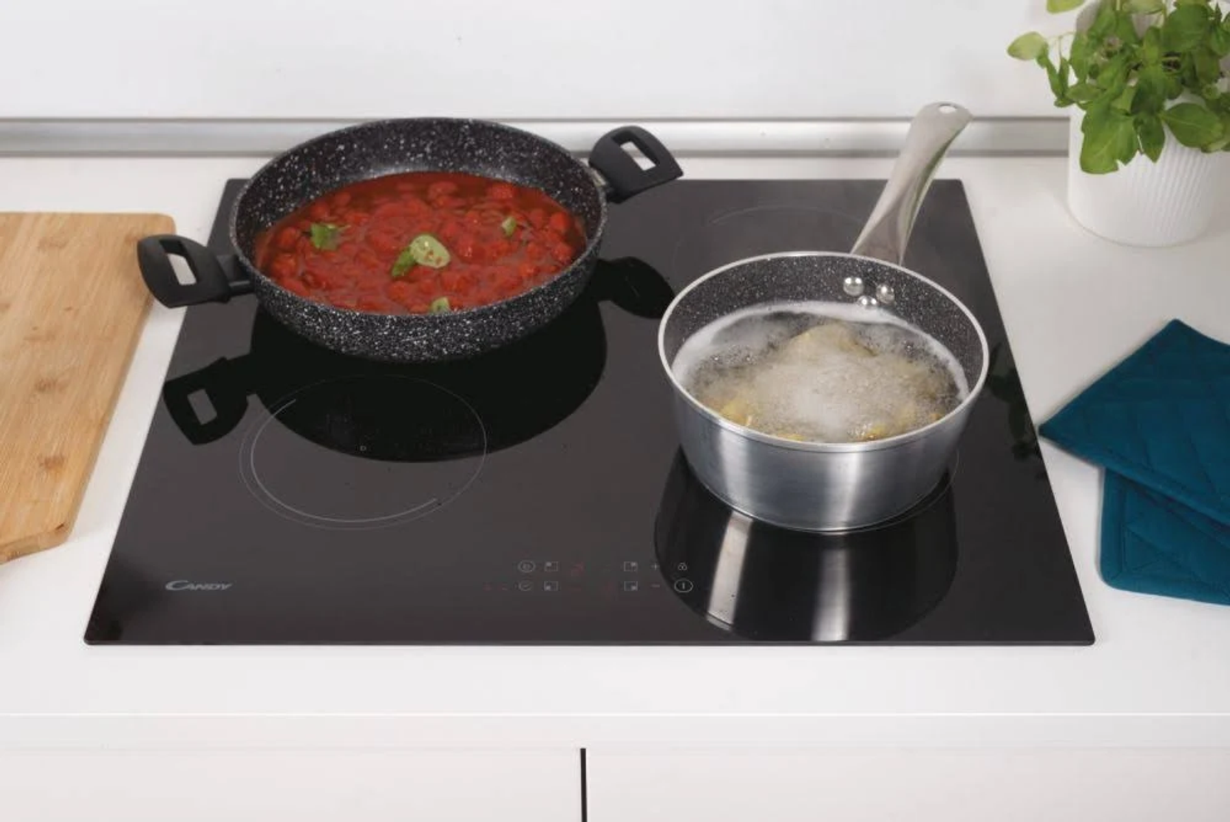 Czarna płyta grzewcza z dwoma garnkami, jeden z sosem pomidorowym, drugi z wrzącym płynem.