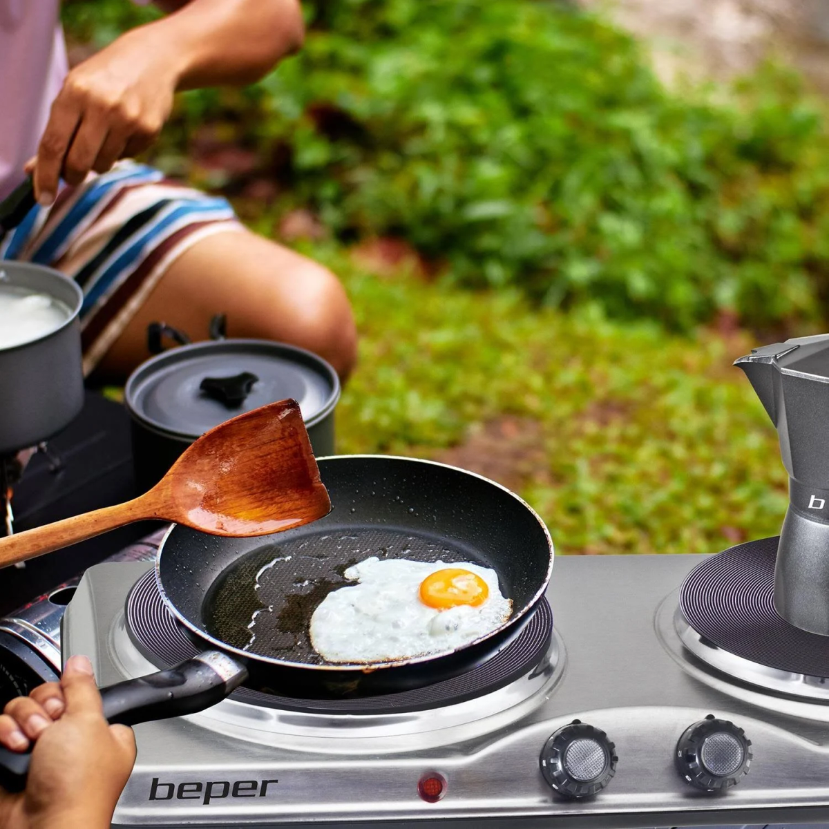 Una persona che cucina un uovo su un fornello elettrico portatile con una spatola di legno.