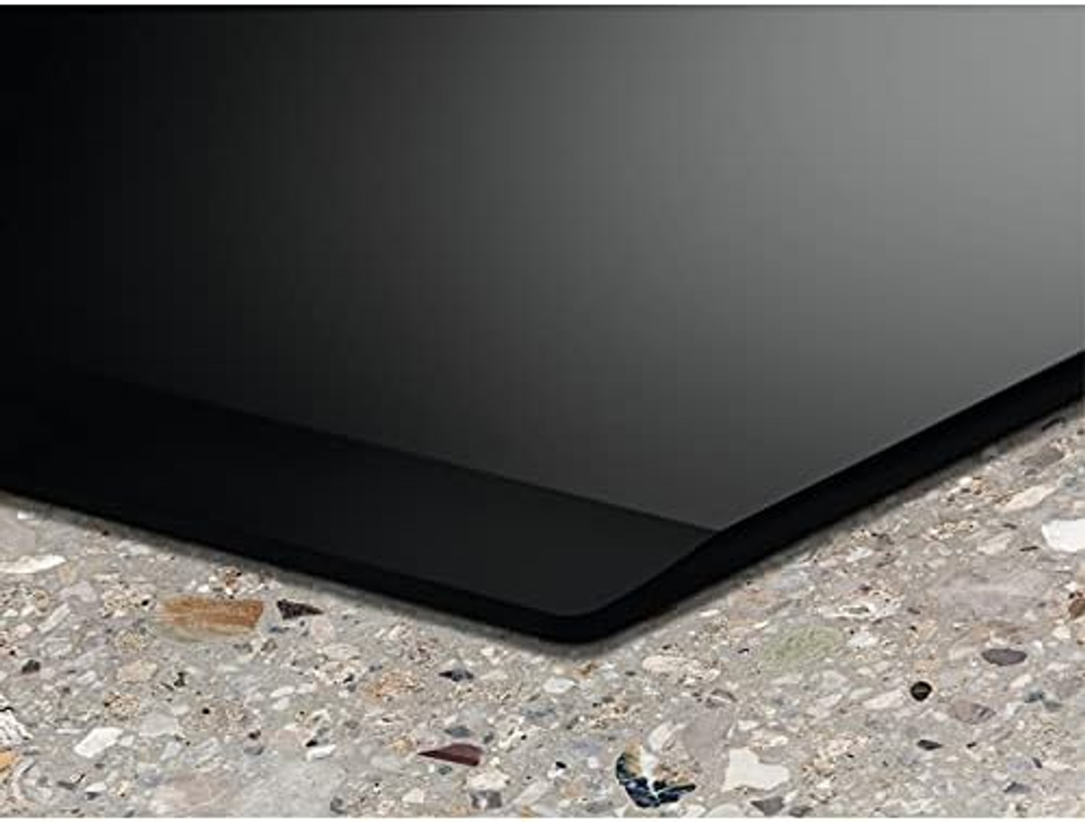 Czarna, błyszcząca powierzchnia na nakrapianym, jasnym blacie, pokazująca róg z lekkim odbiciem.