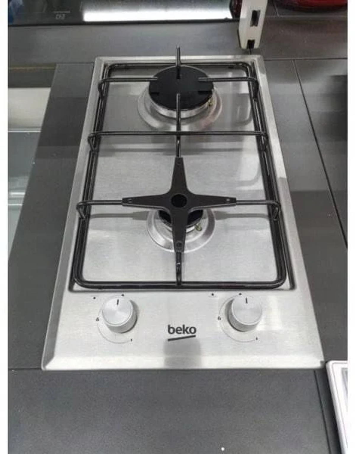 Una encimera de gas de acero inoxidable con dos quemadores, rejillas negras y perillas plateadas.