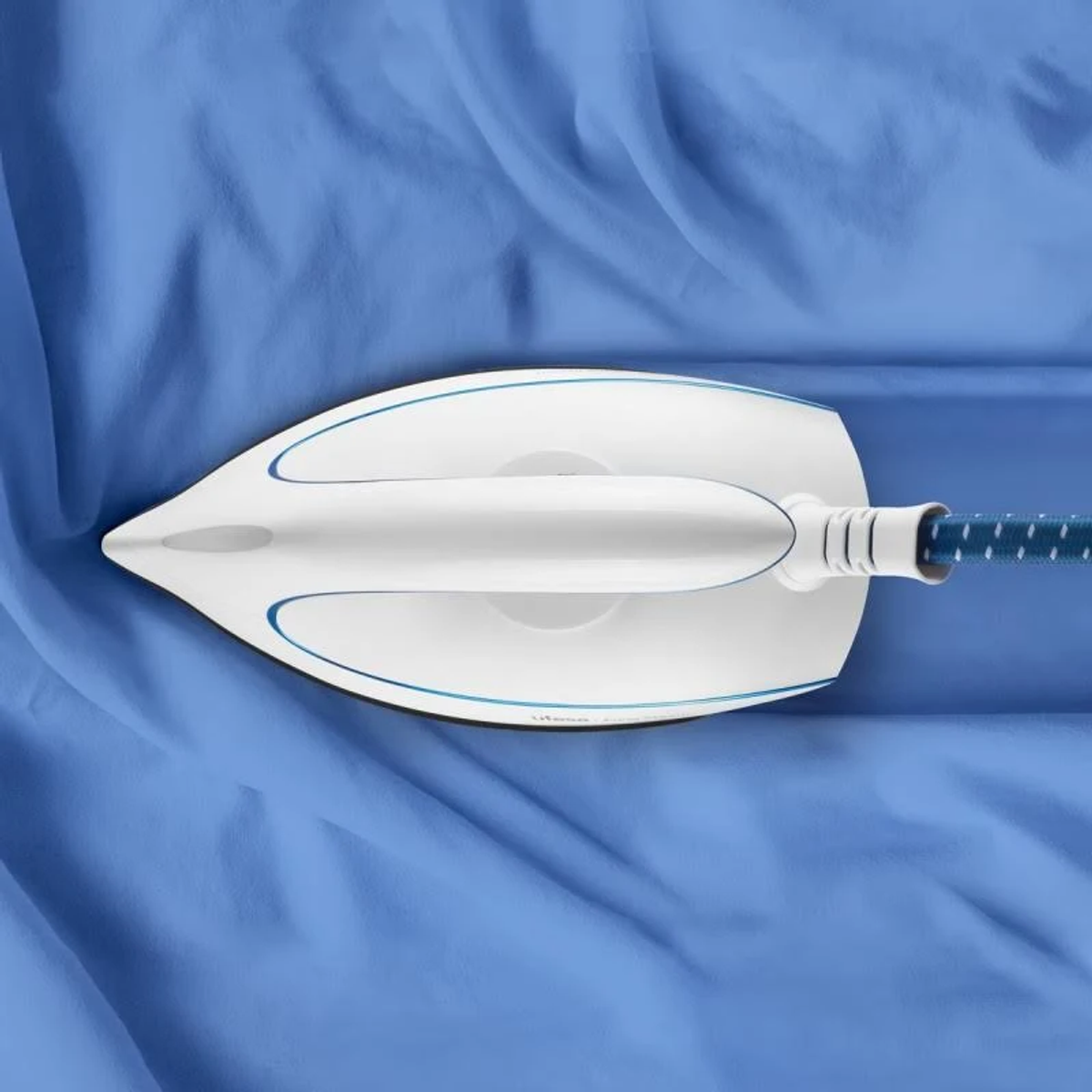 Un ferro da stiro su tessuto blu. Il ferro è bianco con un cavo blu.