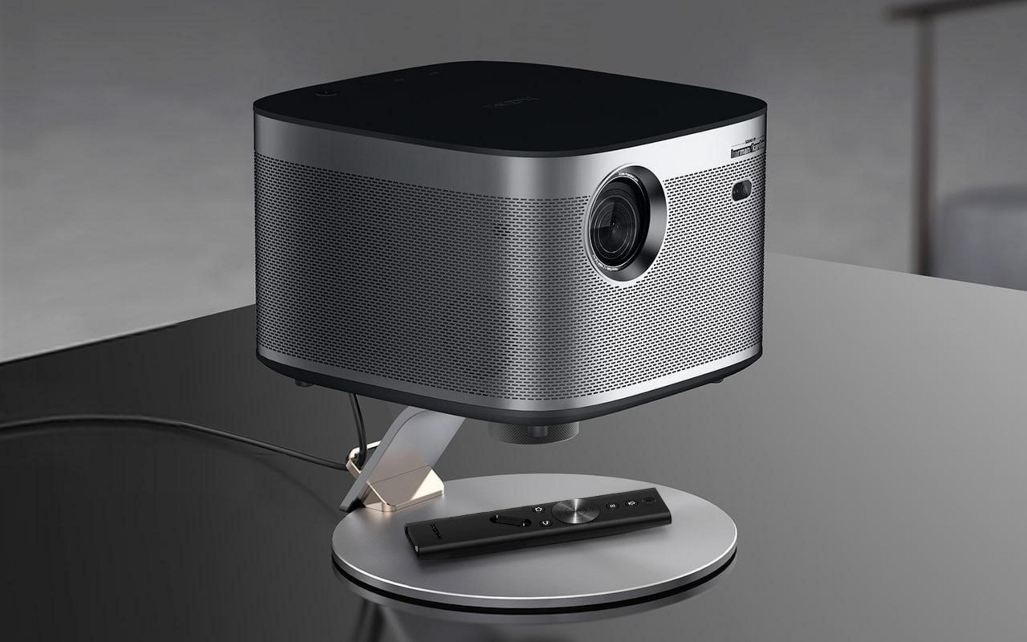 Srebrno-czarny projektor na statywie z pilotem. Projektor jest na stole.