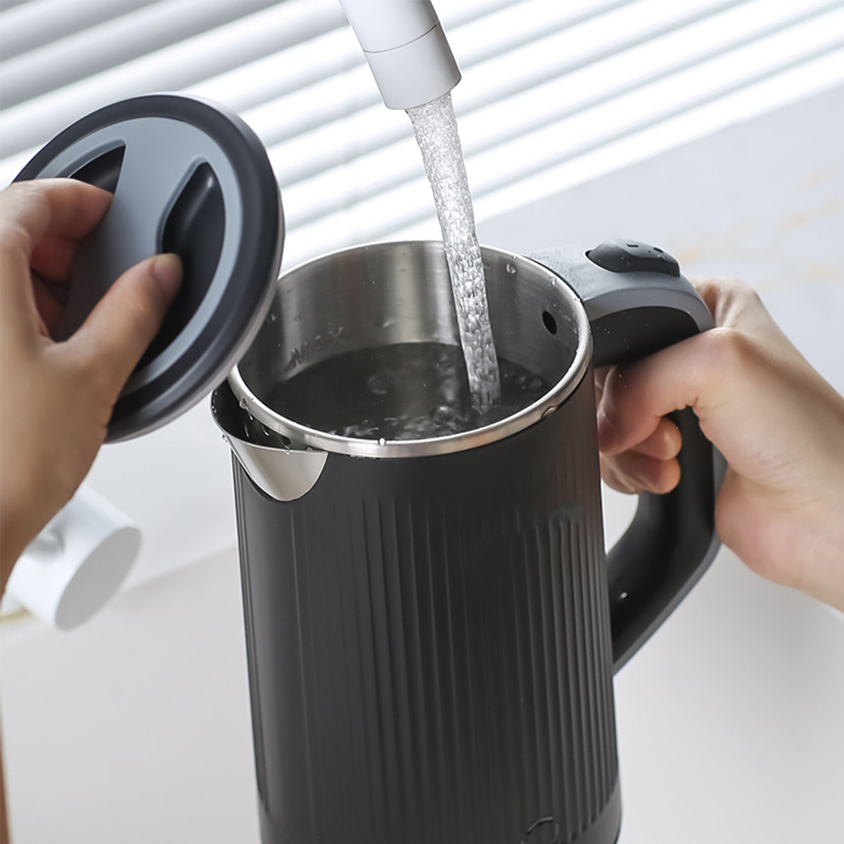 Eine schwarze Teekanne, die von zwei Händen mit Wasser aus einem Wasserhahn gefüllt wird.