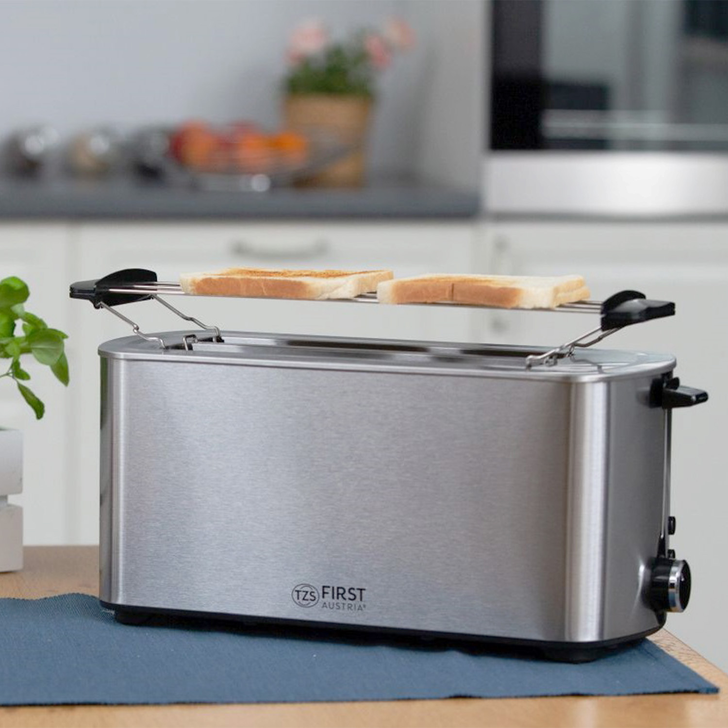 Ein Edelstahl-Toaster mit zwei Brotscheiben auf dem oberen Rost, der auf einem blauen Tisch steht.