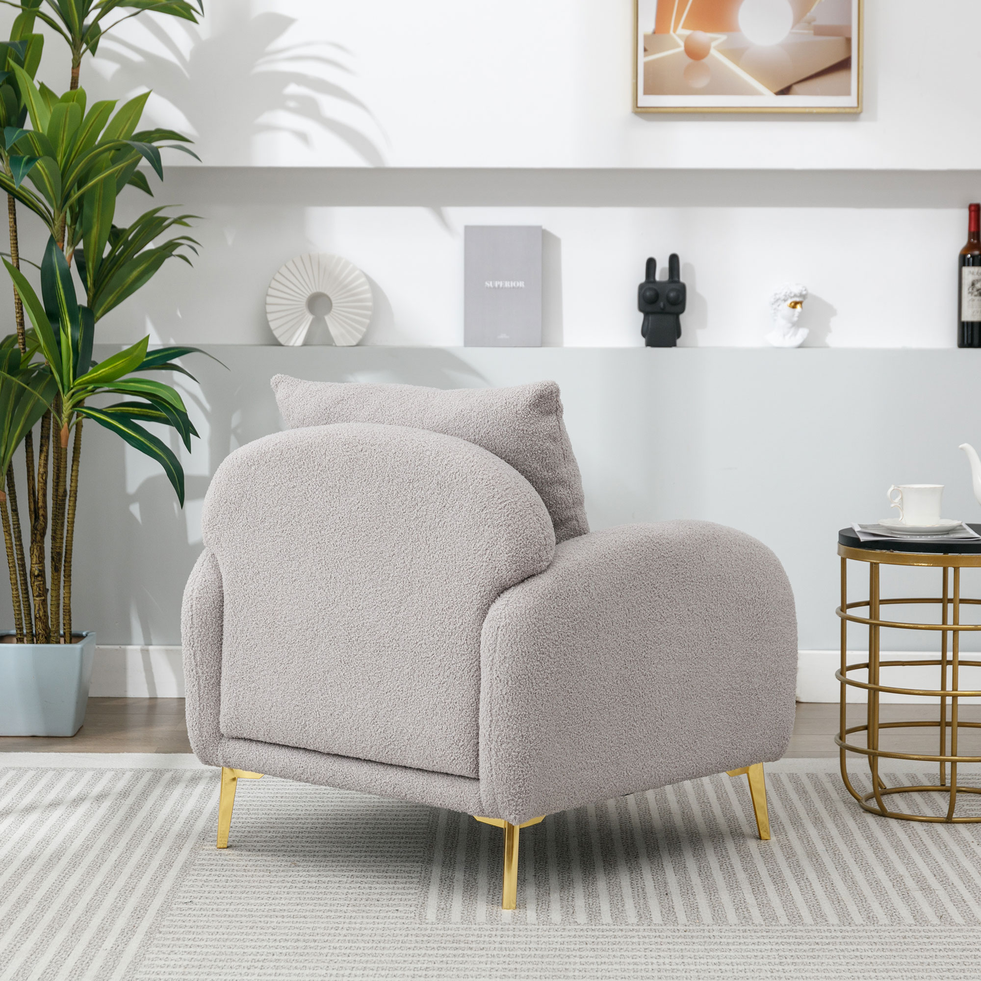 Grauer Teddybär-Sessel mit goldenen Beinen. Ein kleiner Tisch und Deko-Artikel sind im Hintergrund.