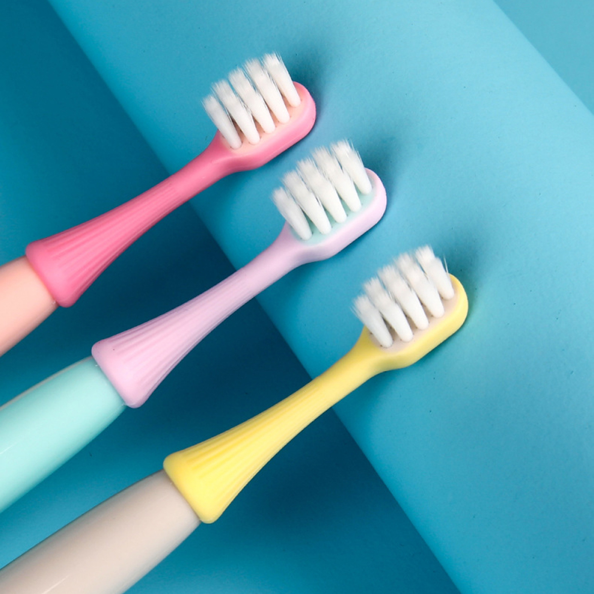 Drei bunte Zahnbürsten in Pink, Lila und Gelb auf einer blauen Oberfläche.
