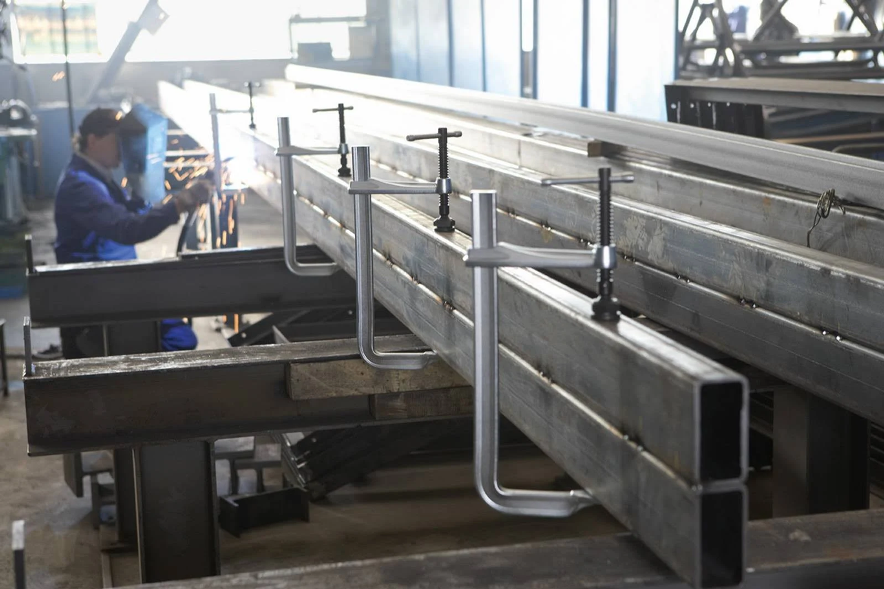 Ein Arbeiter schweißt Metallträger, die auf einem Tisch in einer Werkstatt befestigt sind.