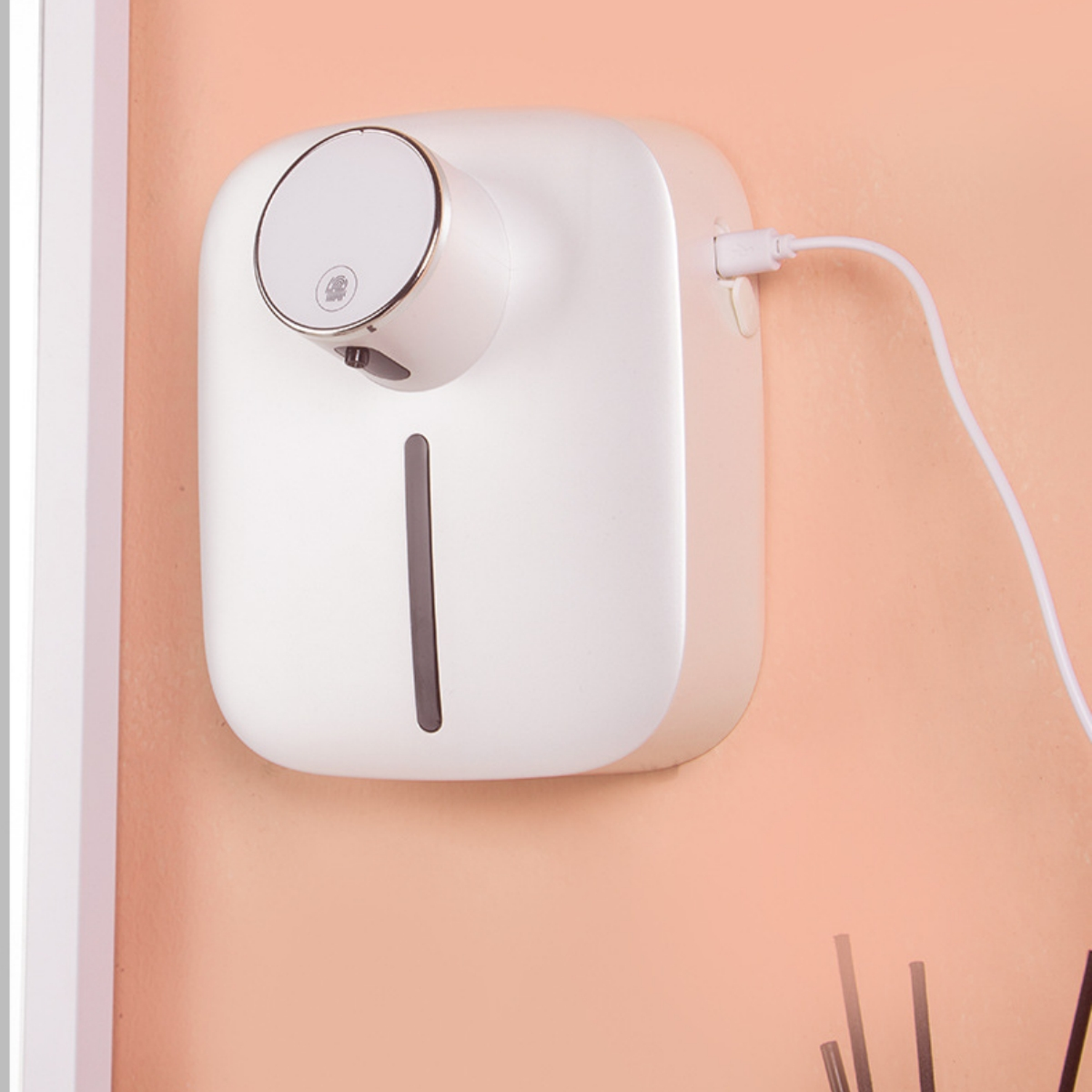 Ein weißer, an der Wand montierter Seifenspender mit rundem Aufsatz, Ausgabebohrung und Ladekabel.