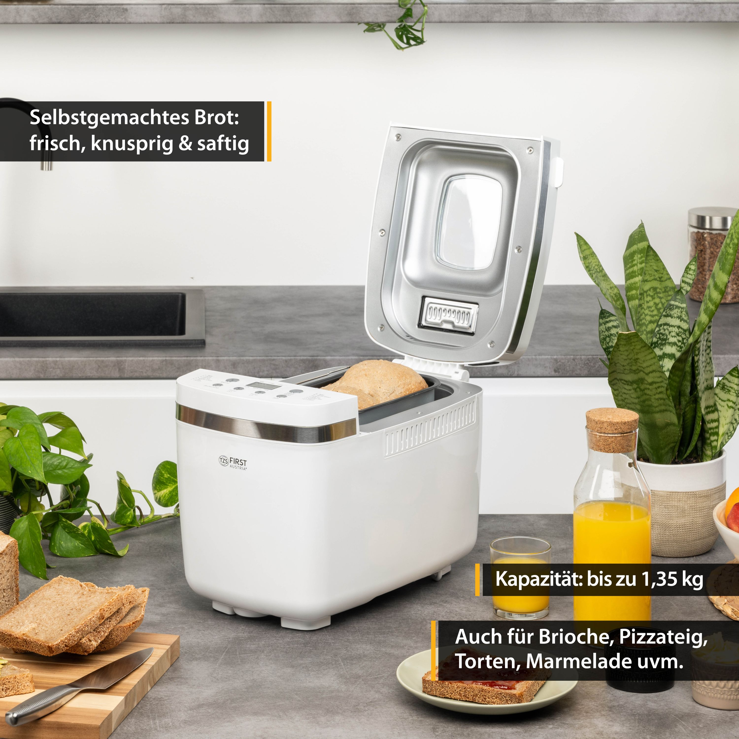 Ein weißer Brotbackautomat, geöffnet, mit Brot darin. Orangensaft und Pflanze rechts.