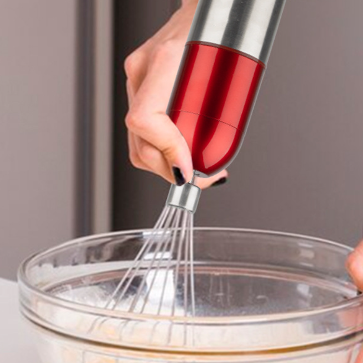 Eine Hand hält einen rot-silbernen Stabmixer über einer Glasschüssel und verrührt einen hellfarbigen Teig.