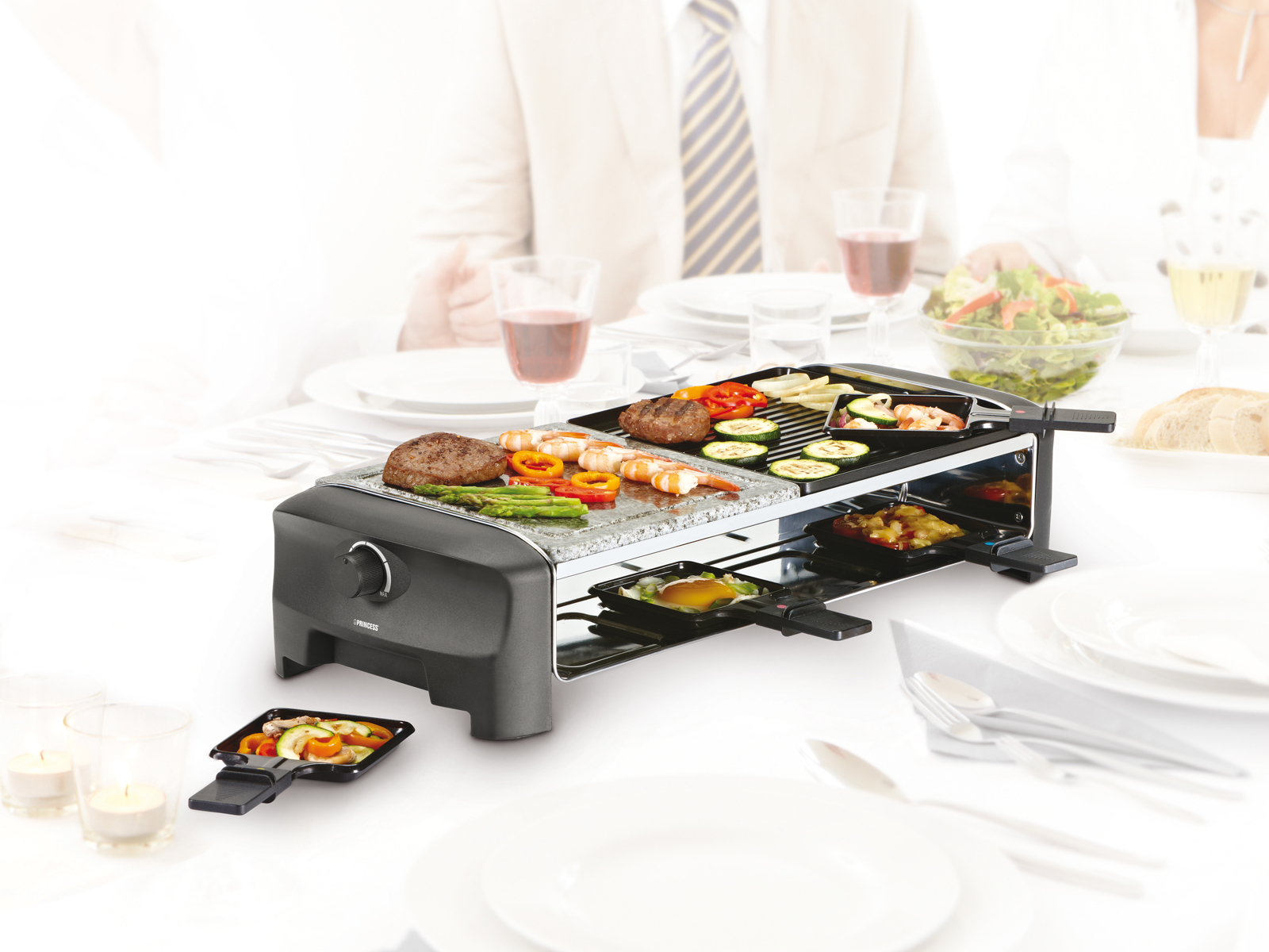 Raclette-Grill mit verschiedenen Lebensmitteln. Personen sind im Hintergrund verschwommen.