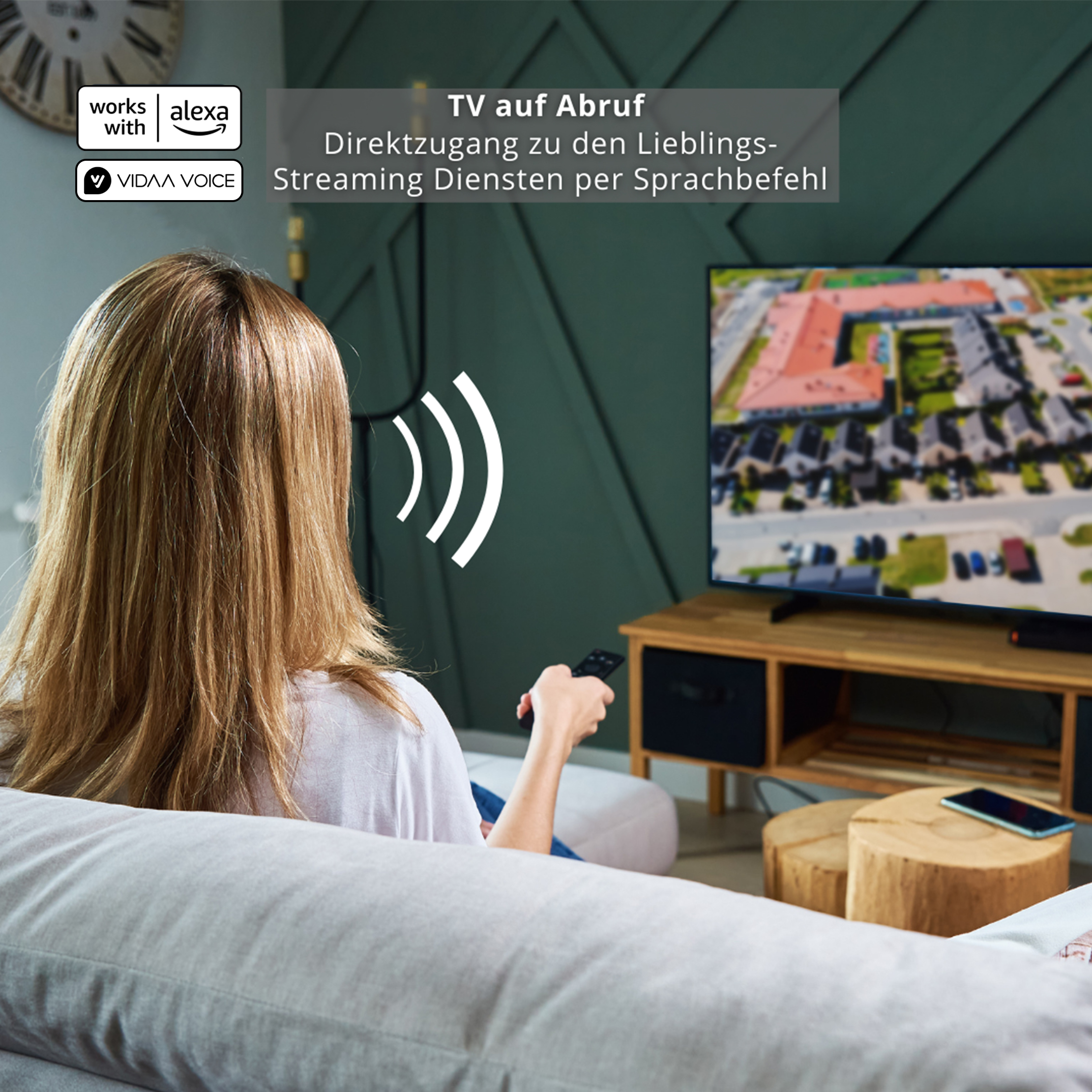 Eine Frau sieht fern. Der Fernseher zeigt eine Stadtansicht. Text sagt 'TV auf Abruf, Streaming-Dienste per Sprachbefehl'.